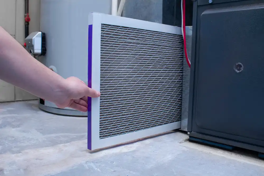 Person inserting or removing a rectangular HVAC air filter from a furnace unit in a utility room.